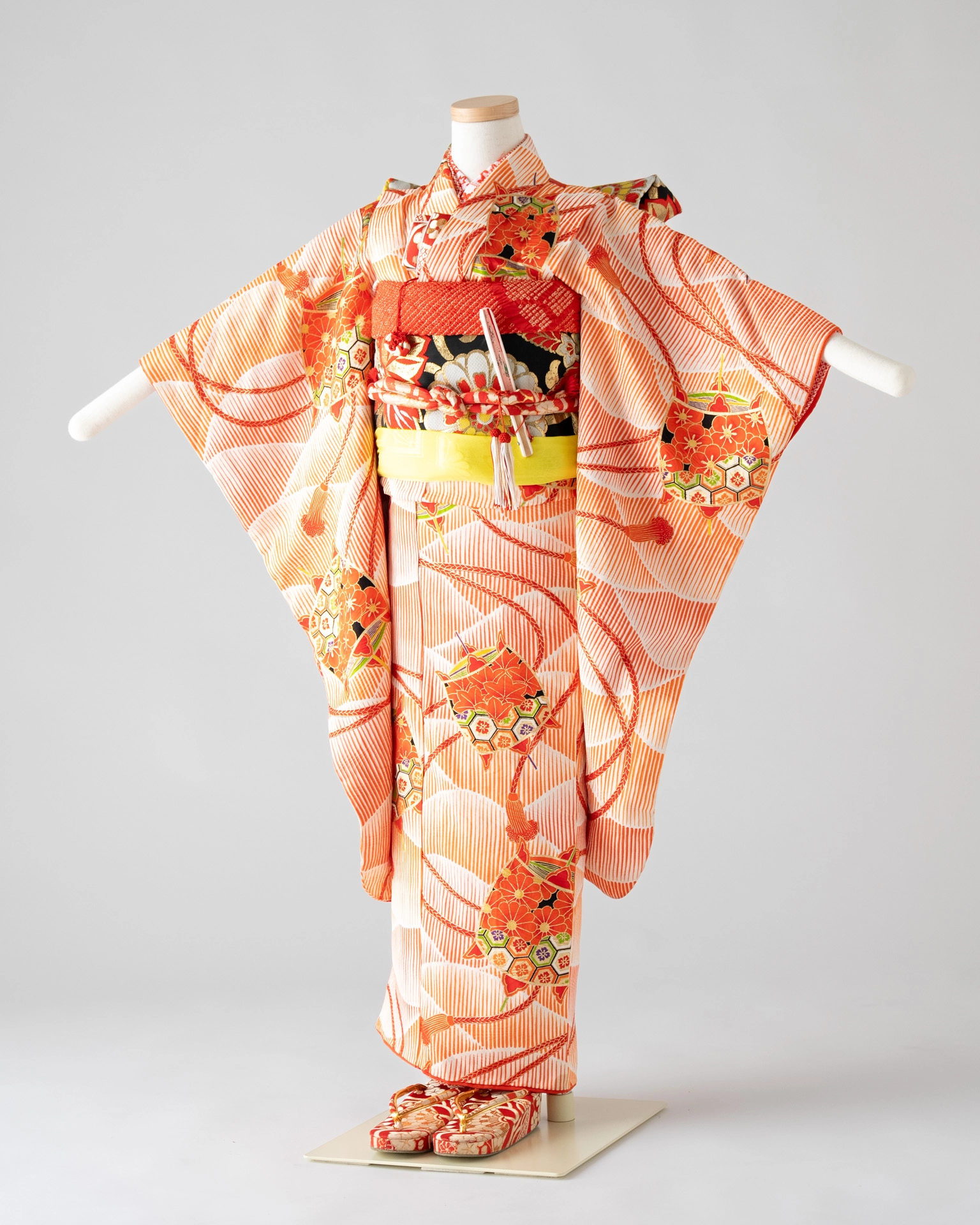 七五三の7歳女の子用、鮮やかな橙色の晴れ着姿。伝統的な文様と帯、小物が美しくコーディネートされている。